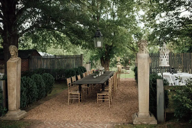 wedding reception table with flowers and gold chairs at Hedge Farms wedding venue in Red Banks, MS with dress and suit on doors photo by The Warmth Around You